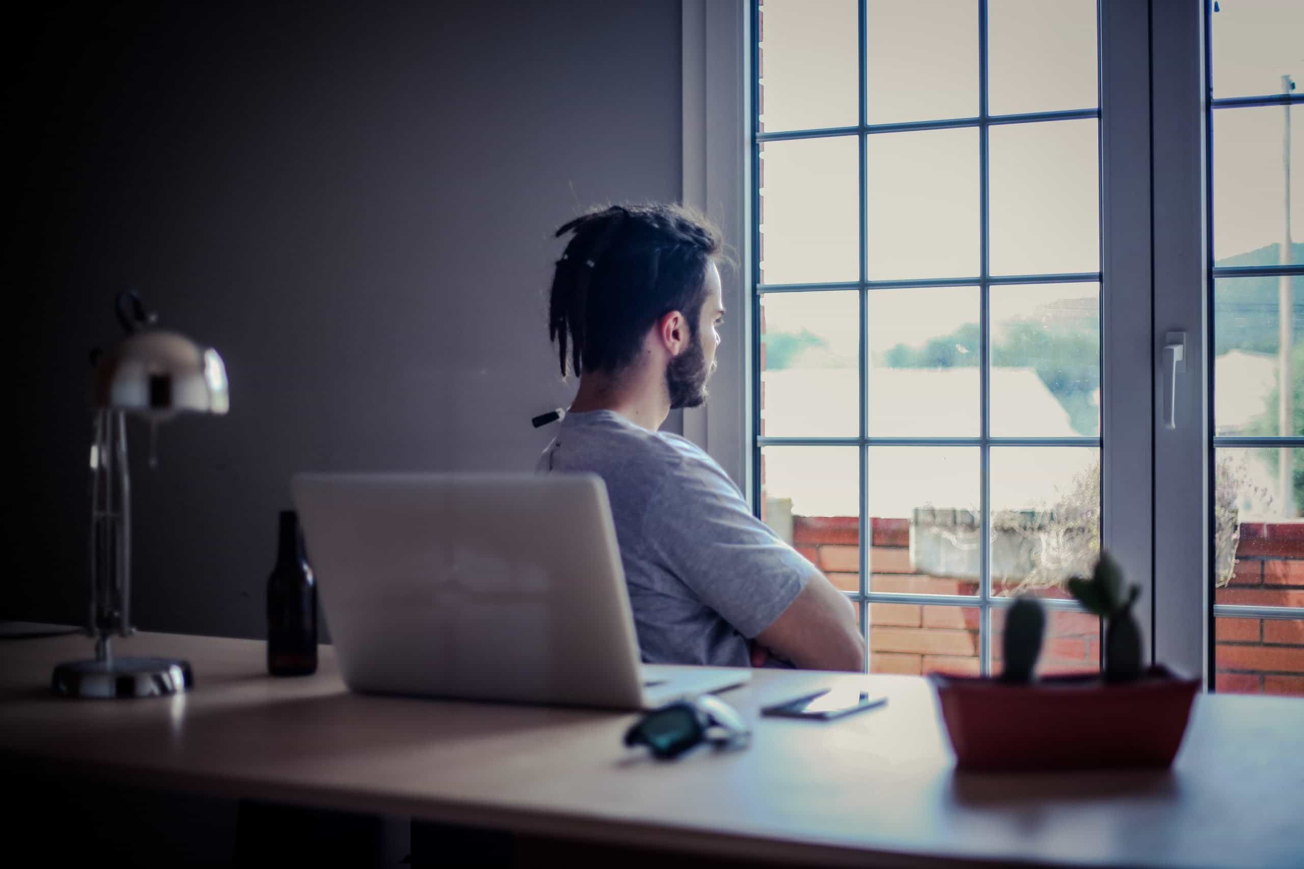 Man sitting at desk looking out of window being reflective in thought